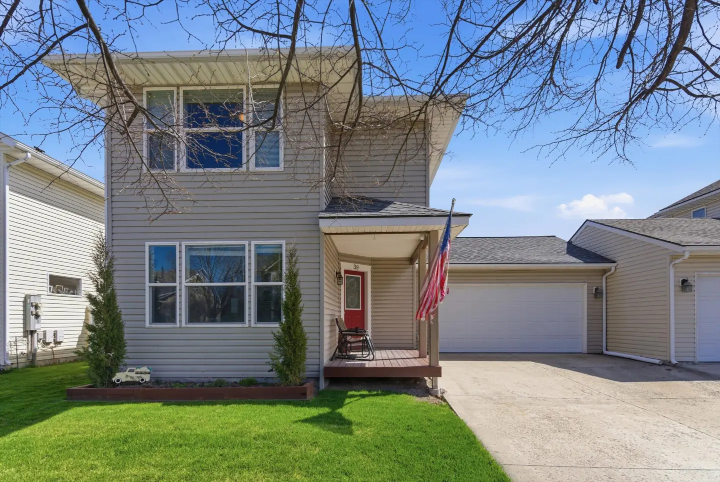 Two-story house with gray siding, a red front door, and an American flag on the porch. Green lawn and blue sky.