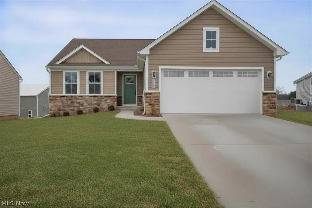 A single-story house with tan siding, a brown roof, a green front door, and a white garage door.
