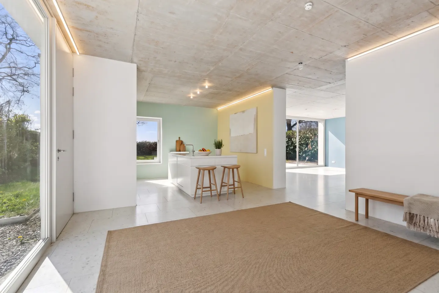 Bright, modern home interior with a tan rug, white walls, and a kitchen island with wooden stools. A bench sits against the wall.