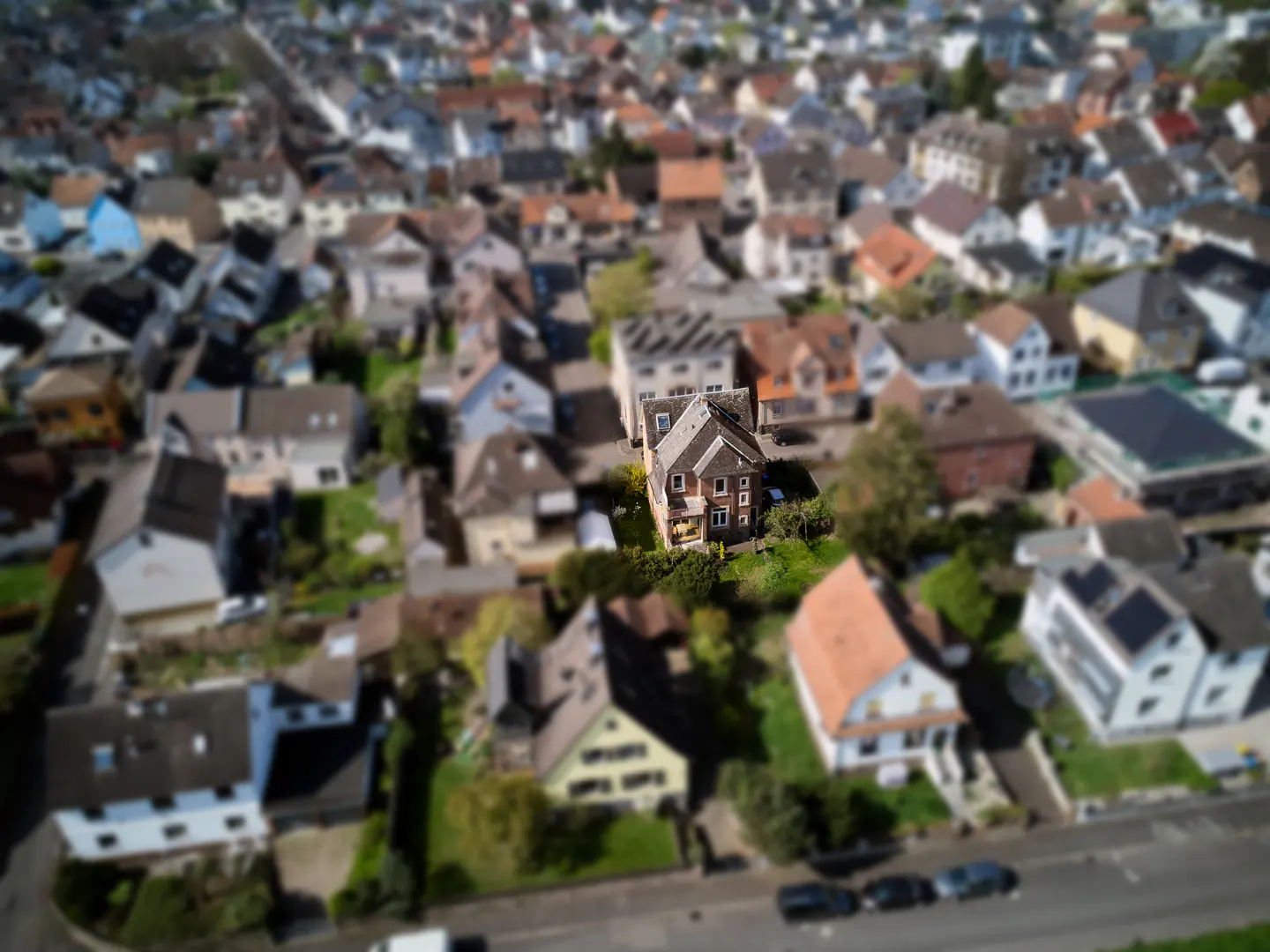 Aerial view of a brown house in a residential neighborhood, with a tilt-shift effect blurring the surrounding homes.