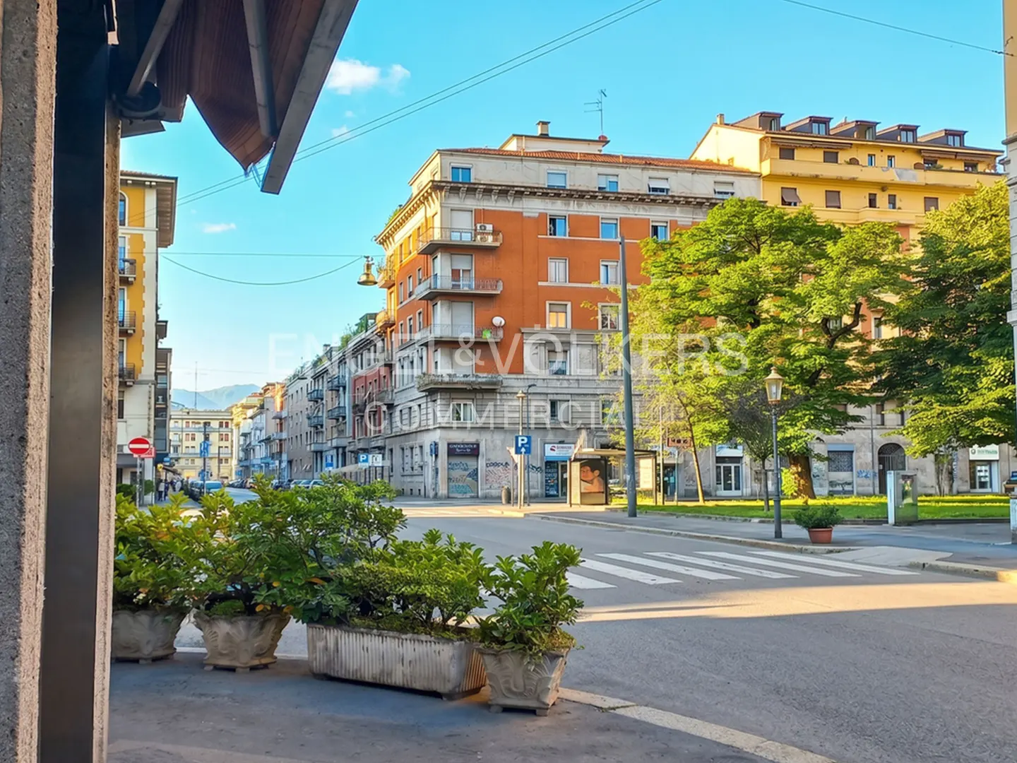 Street view of European city with orange and yellow buildings, crosswalk, and planters.