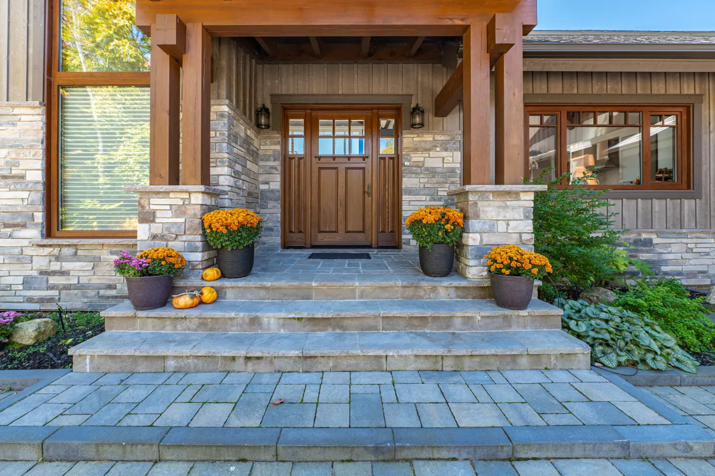 Front entrance of a house with stone steps, wooden door, and orange flowers in pots. Pumpkins decorate the steps.