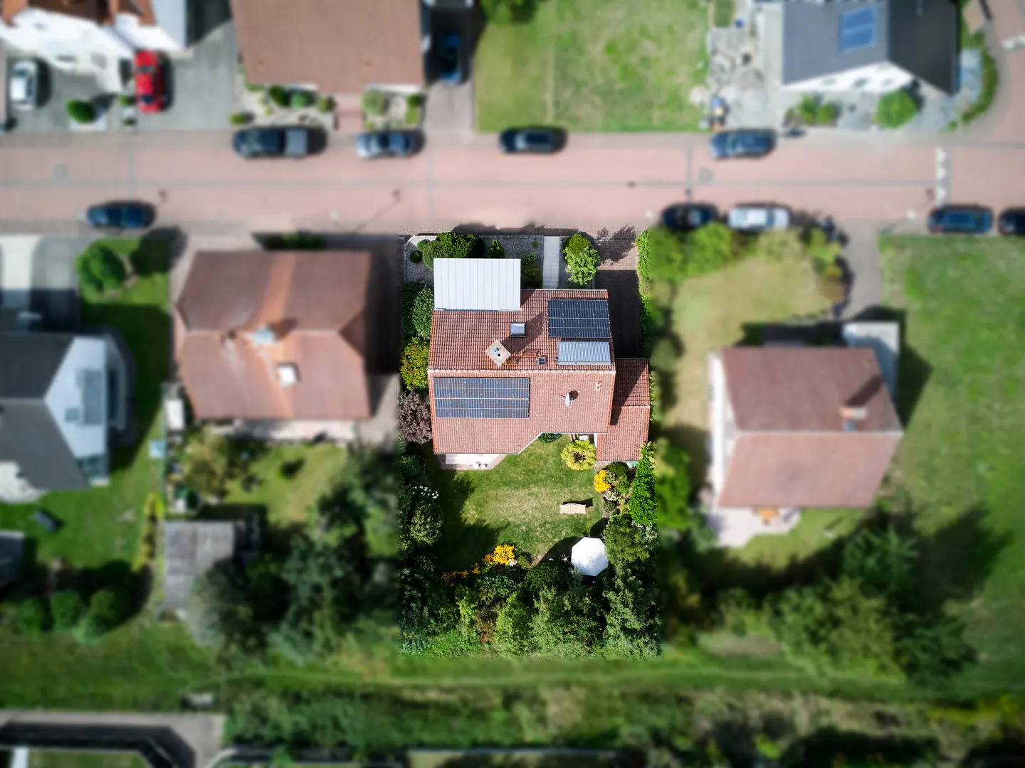 Aerial view of a house with solar panels on the roof, surrounded by a green lawn and trees.