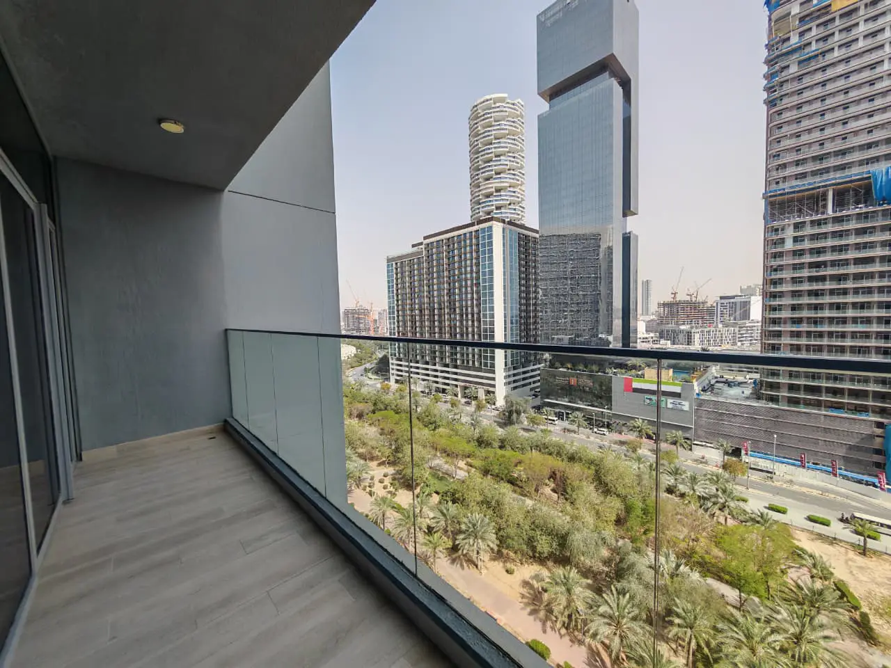 Balcony view of Dubai skyline. Glass railing overlooks trees and buildings. Gray tiled floor.