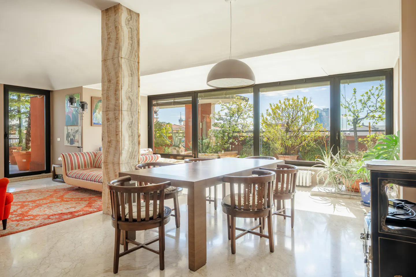 Bright dining room with a wooden table, chairs, and a large window overlooking a terrace with plants and city views.