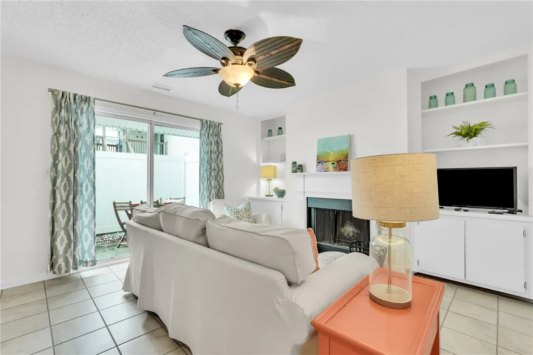 Bright living room with white sofa, fireplace, and built-in shelves. A ceiling fan hangs above, and sliding glass doors lead to a patio.