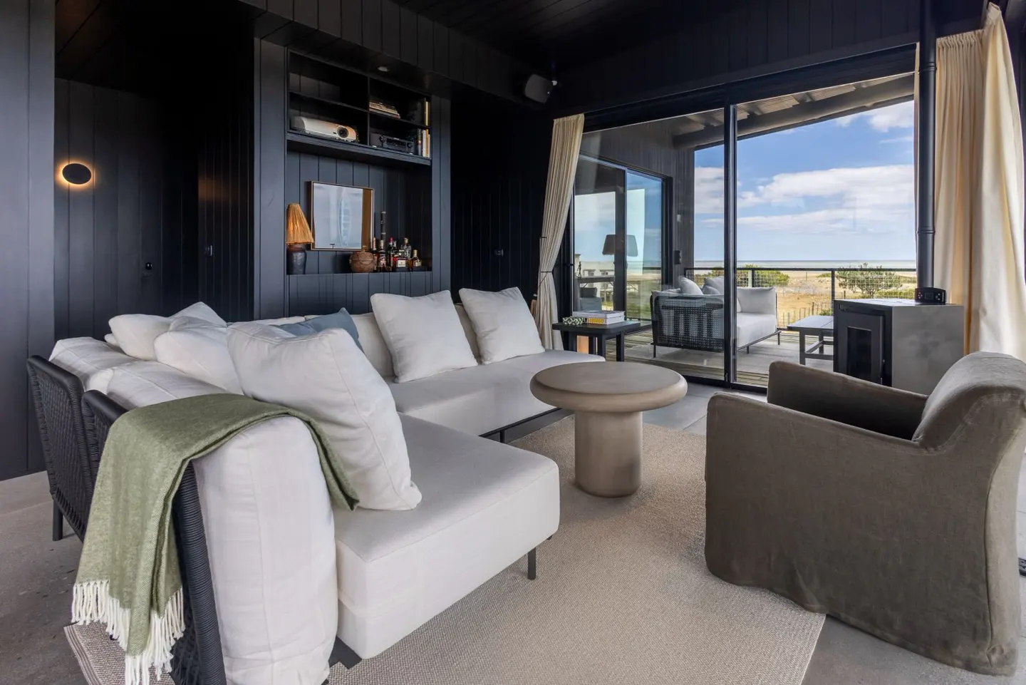 Living room with black walls, white sofa, and a view of the beach through sliding glass doors. A green throw blanket is draped over the sofa.