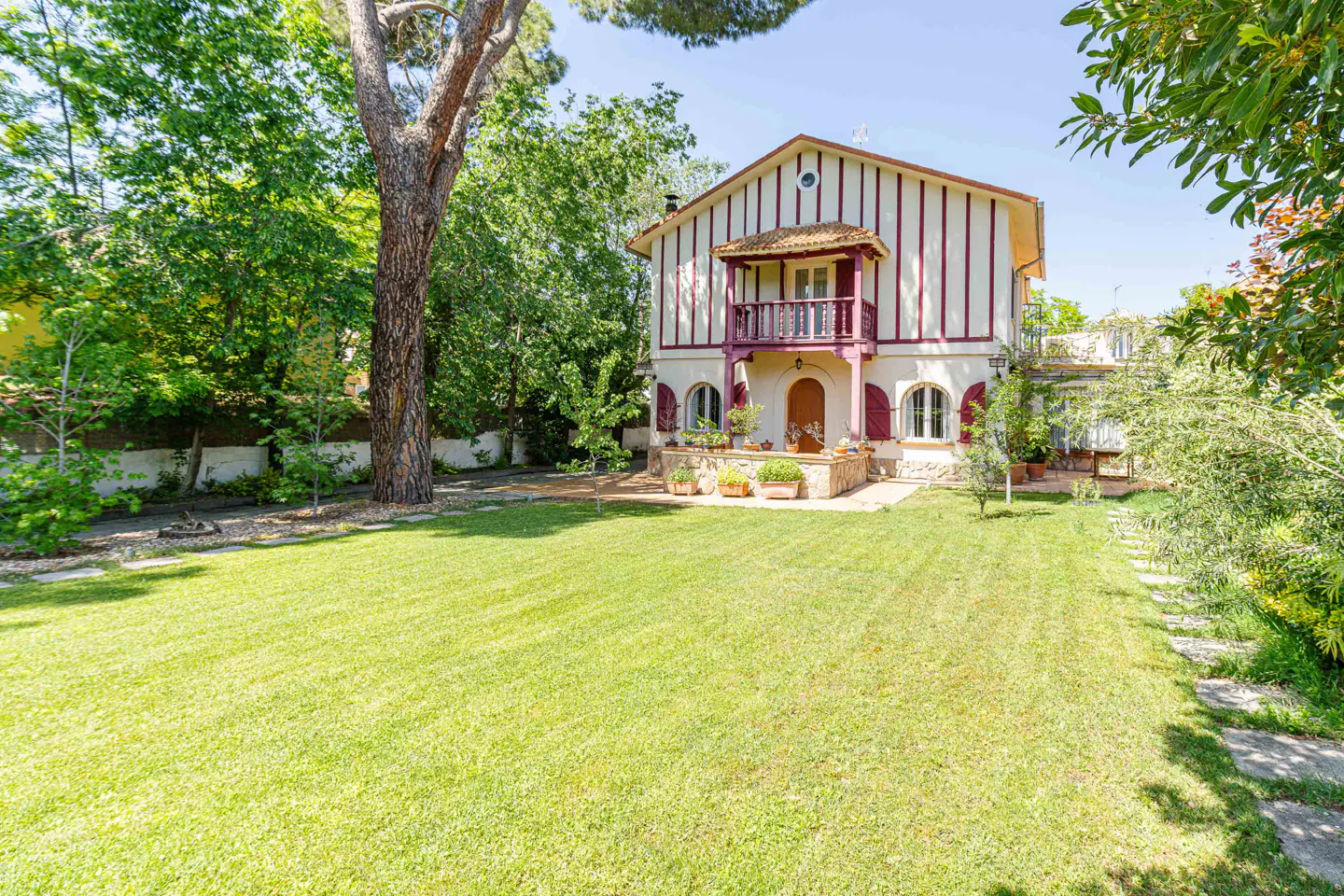 Two-story house with white and red vertical stripes, balcony, red shutters, and a large green lawn.