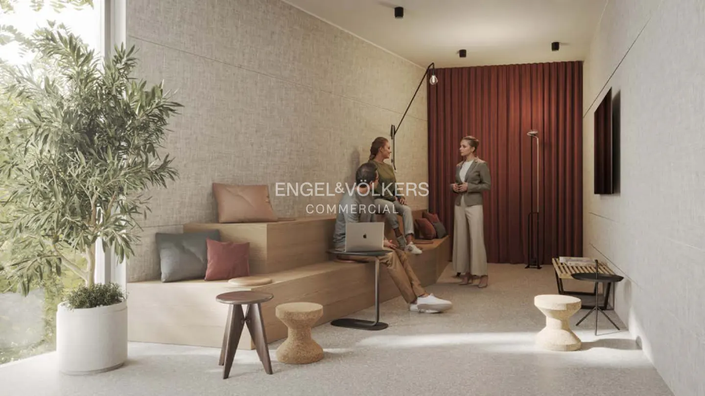 Engel & Völkers commercial space with three people sitting and talking. A man is working on a laptop. There is a large plant in the corner.