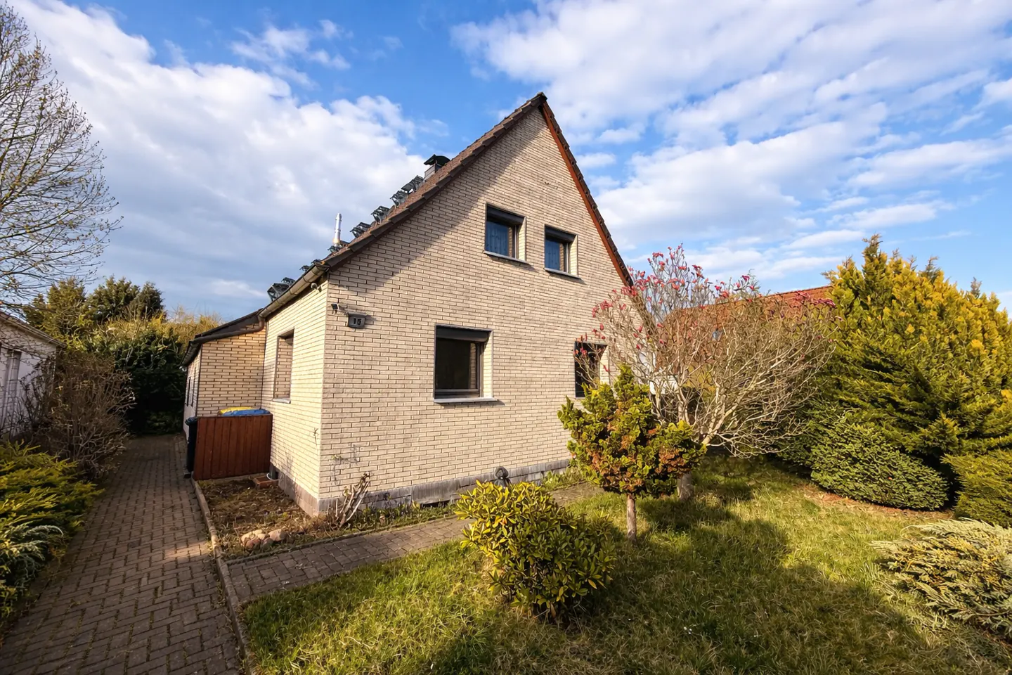 A one-and-a-half-story beige brick house with a brown roof, green lawn, and blue sky.