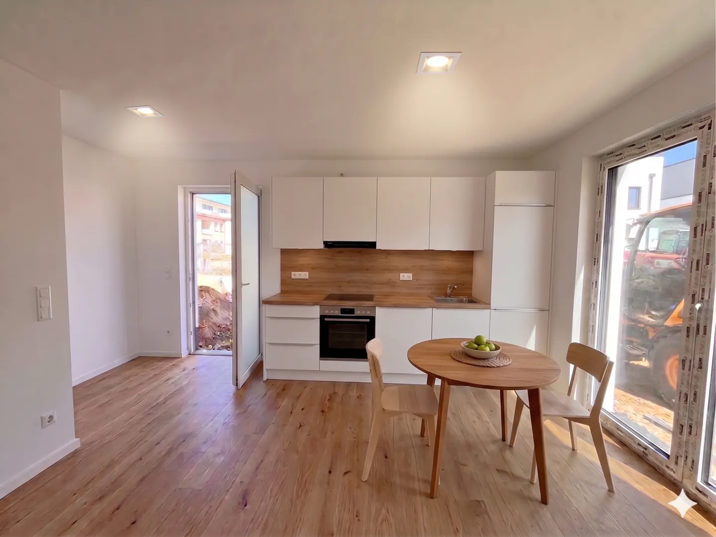 Bright kitchen with white cabinets, wood countertops, and a round table with two chairs. A tractor is visible through the window.
