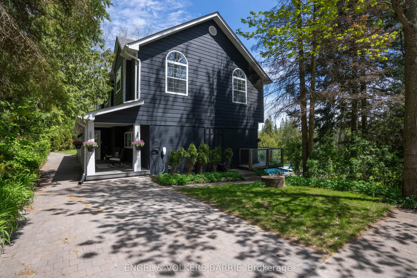 A two-story house with dark siding, white trim, arched windows, and a covered porch surrounded by trees.
