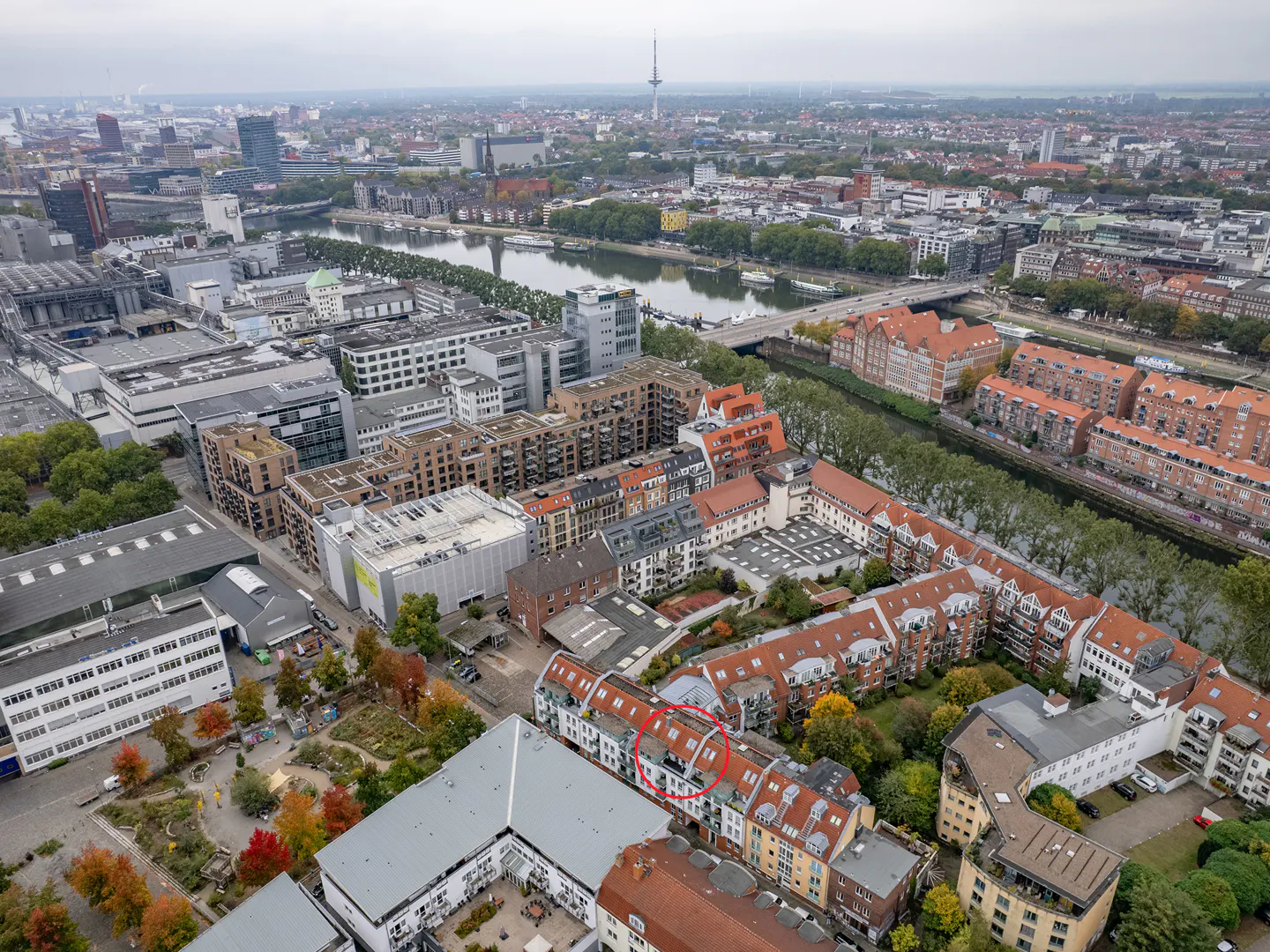 Aerial view of a city with a river, buildings, and a TV tower in the background. The focus is on a row of houses with red roofs.
