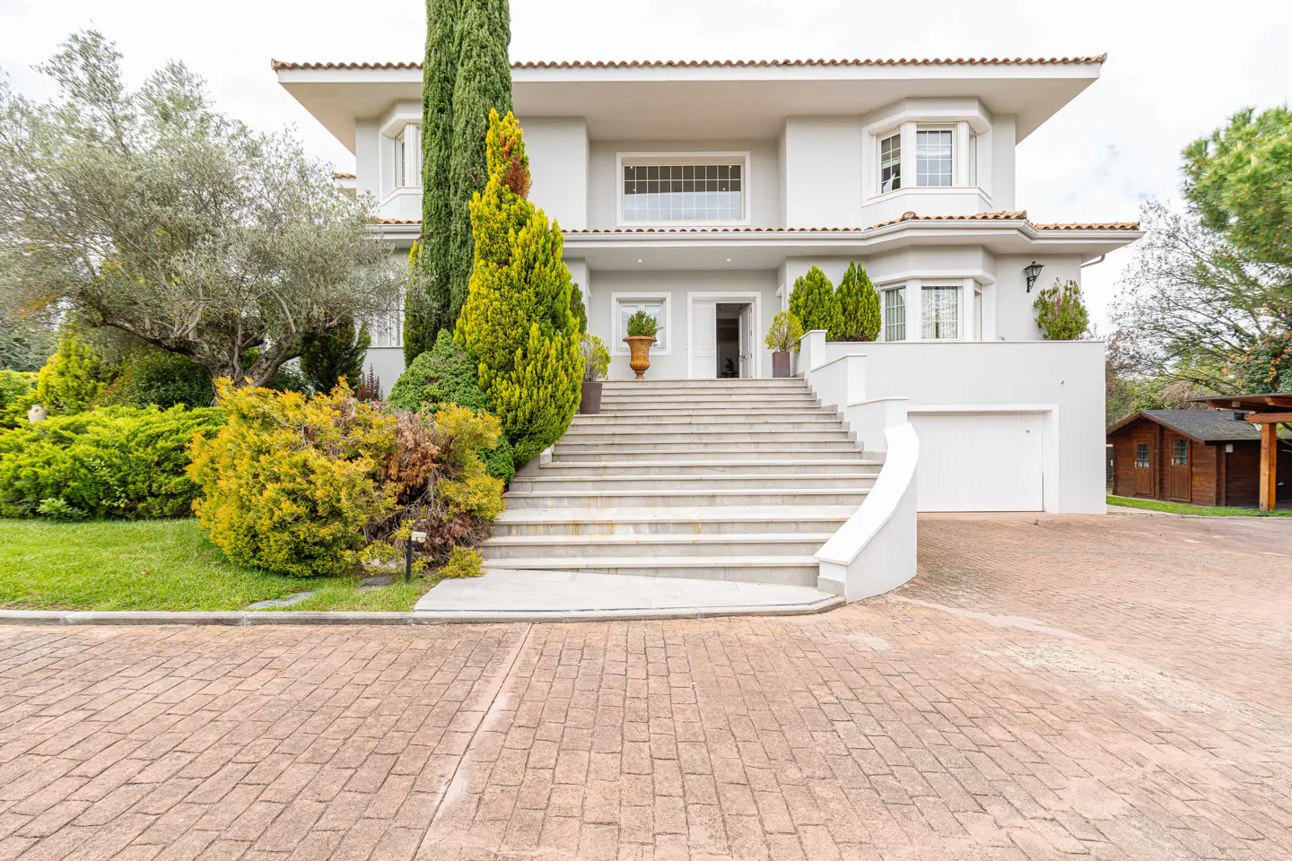 A two-story gray house with a red tile roof, a white garage door, and a long staircase leading to the front door.