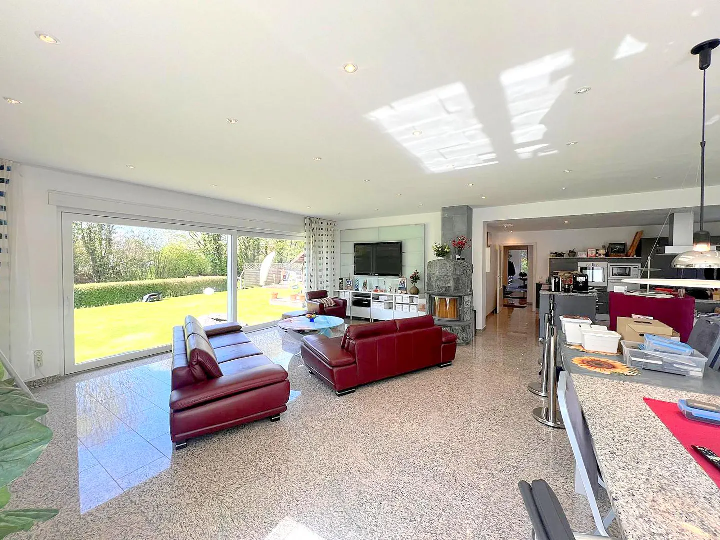 Bright living room with red leather sofas, stone fireplace, TV, and large sliding glass doors to a green lawn.