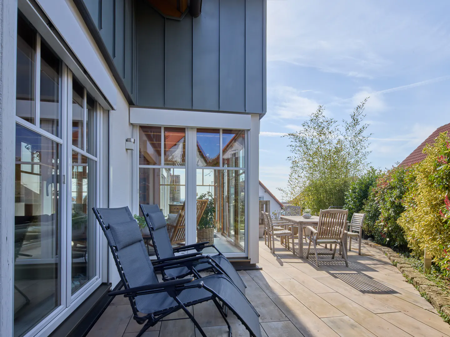 Outdoor patio with two gray lounge chairs, a wooden table and chairs, and a view of the sky.
