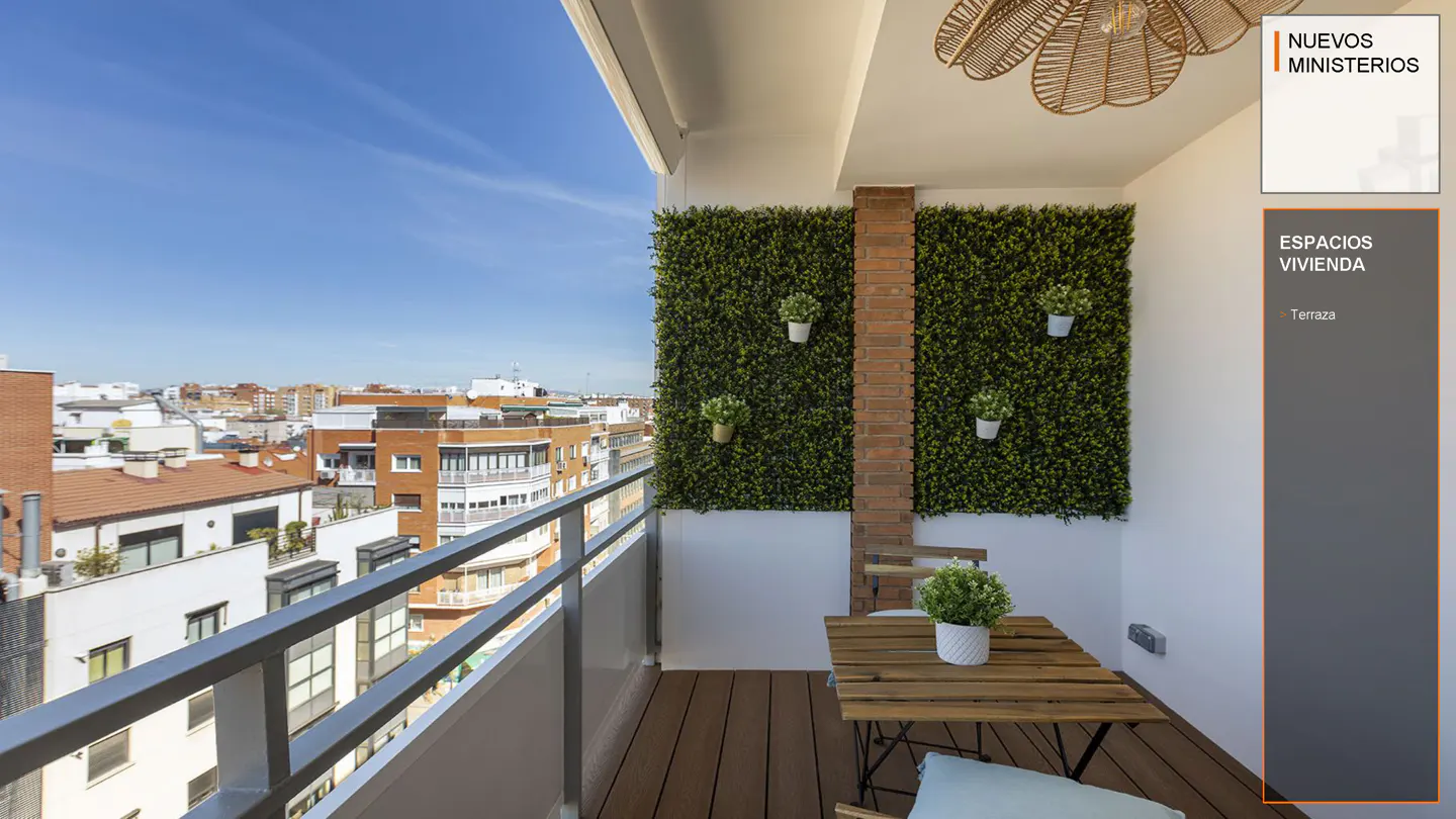 A balcony with a wooden table and chairs, a green wall with plants, and a city view.