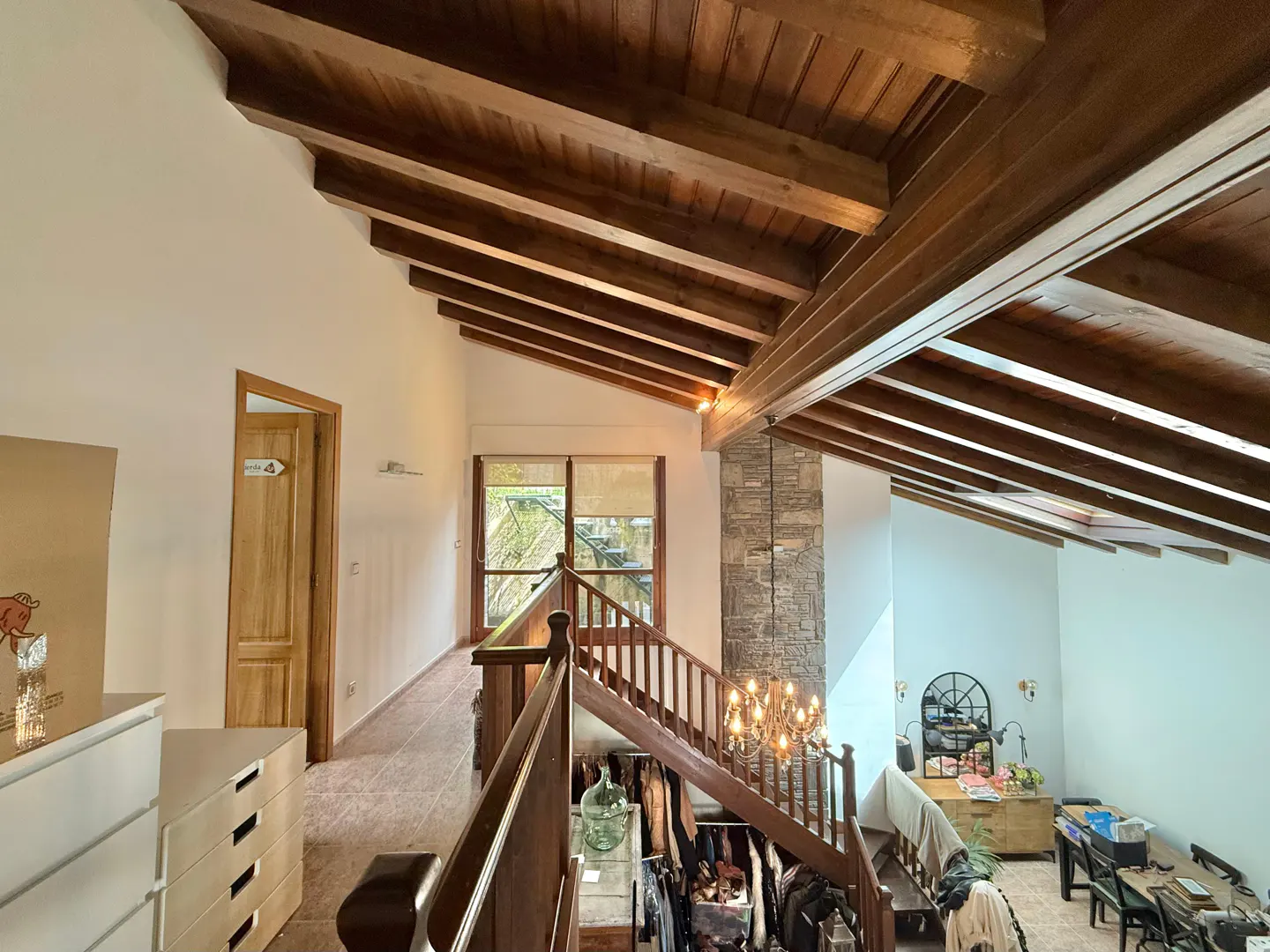 Interior view of a home featuring a wooden beamed ceiling, stone pillar, and staircase with wooden railings.