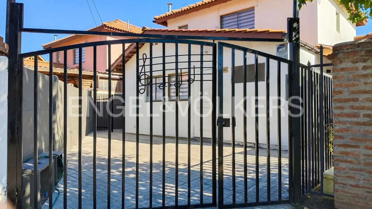 Black metal gate with musical notes design, leading to a white house with a brown roof. Engel & Volkers logo visible.