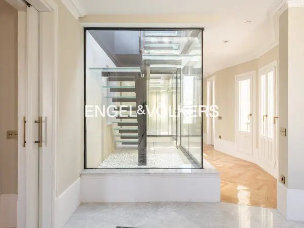 Modern hallway with a glass-enclosed staircase featuring floating glass steps over a white pebble floor.