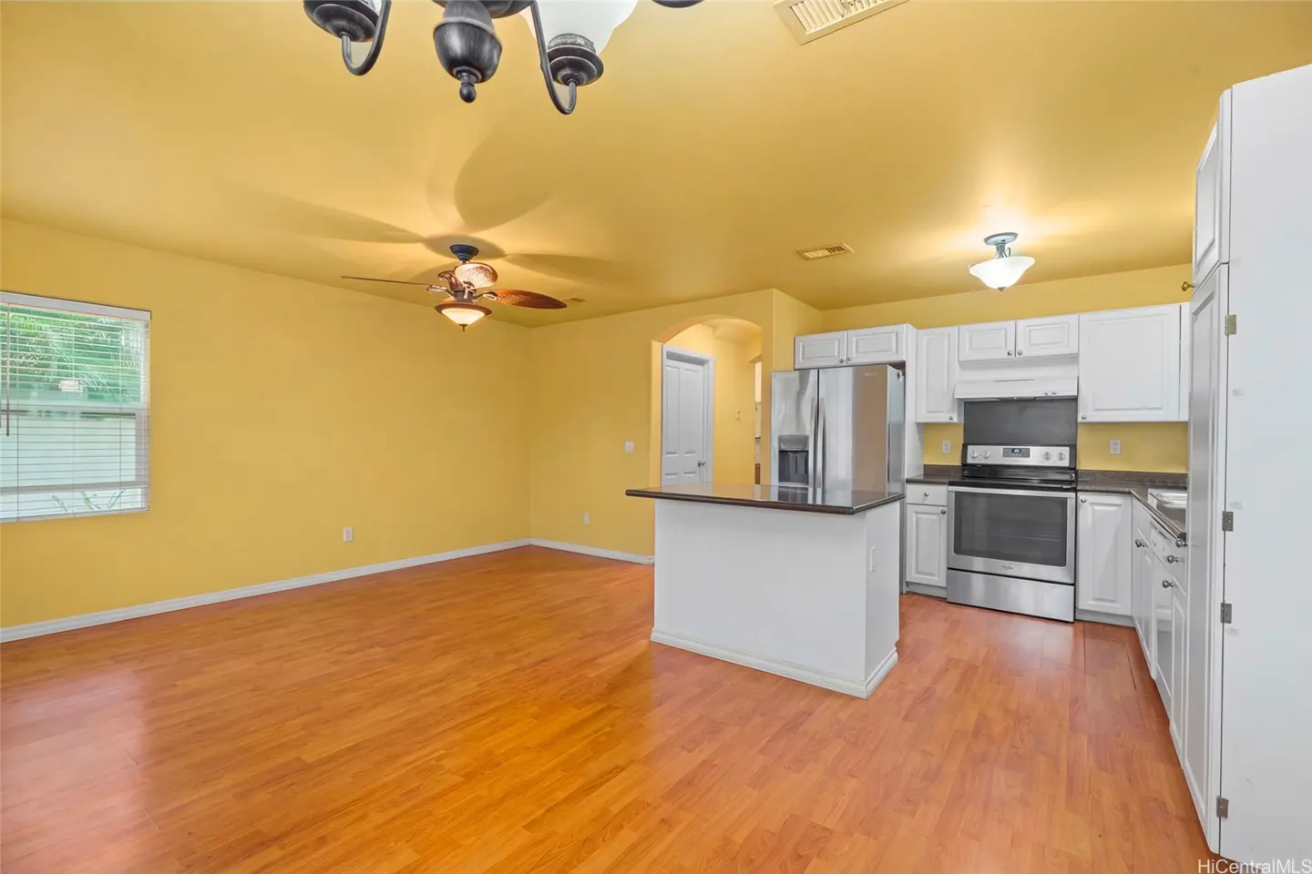 Open-concept living space with yellow walls, wood floors, and white kitchen. Stainless steel appliances and island with dark countertop.
