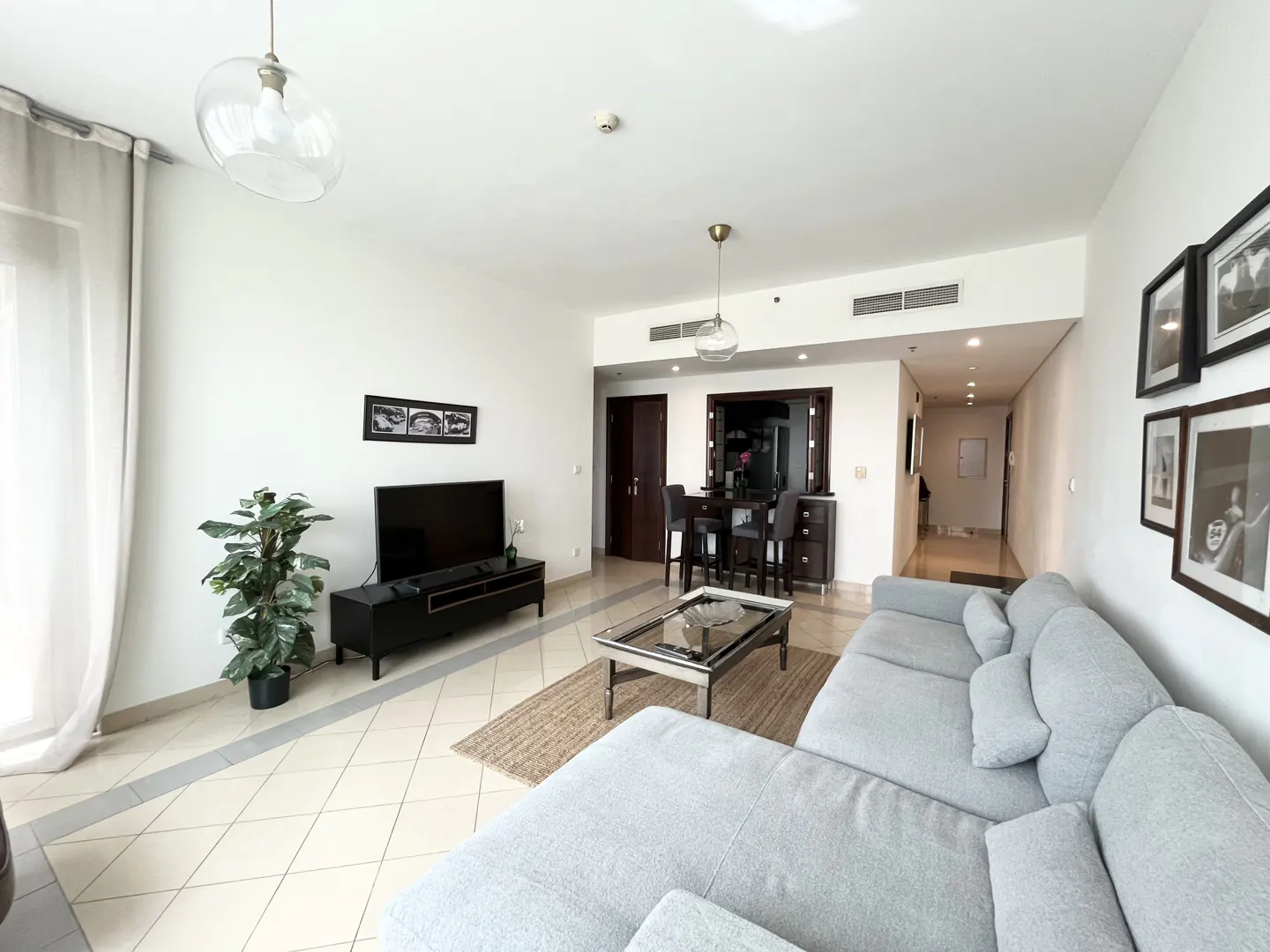 A bright living room with a gray sectional sofa, TV, bar stools, and framed photos.