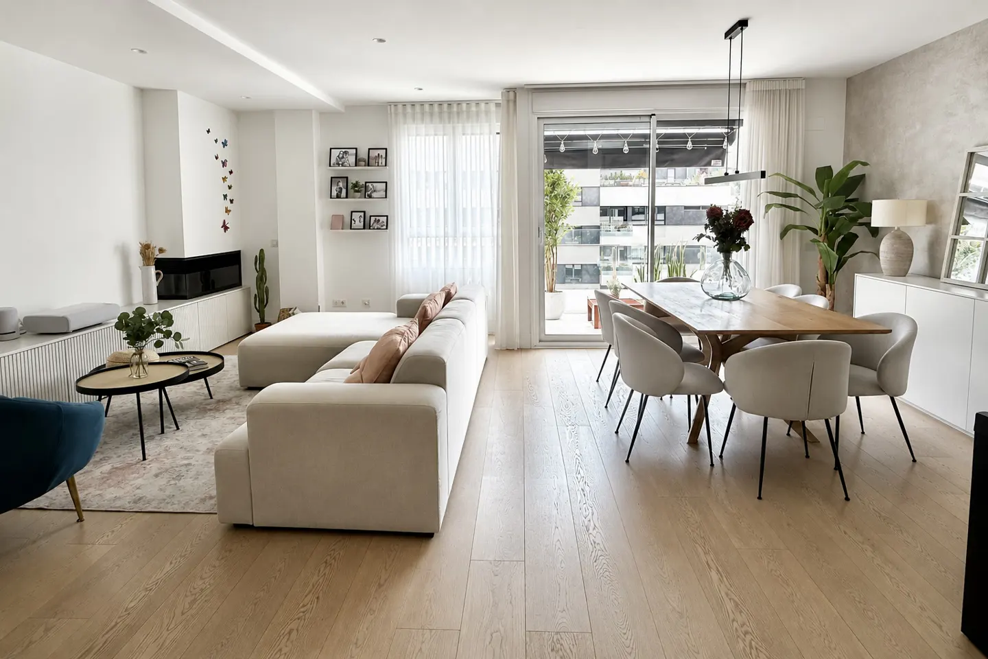 Bright, modern living room with a beige sectional sofa, wood dining table with six chairs, and a sliding glass door to a balcony.