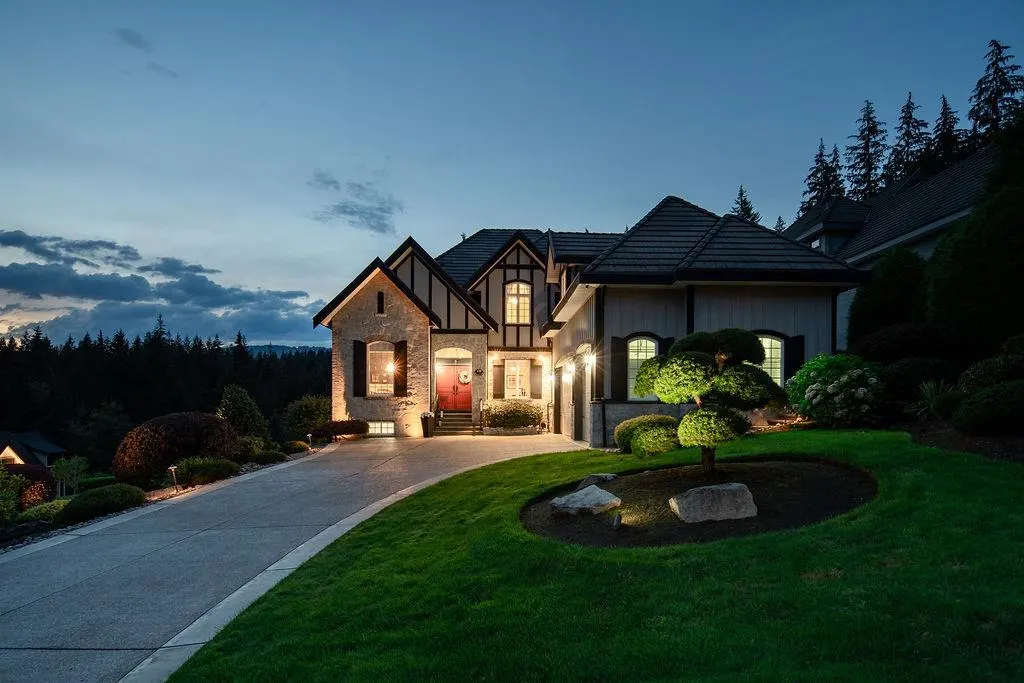 A two-story house with a red door, black shutters, and a gray driveway at dusk.