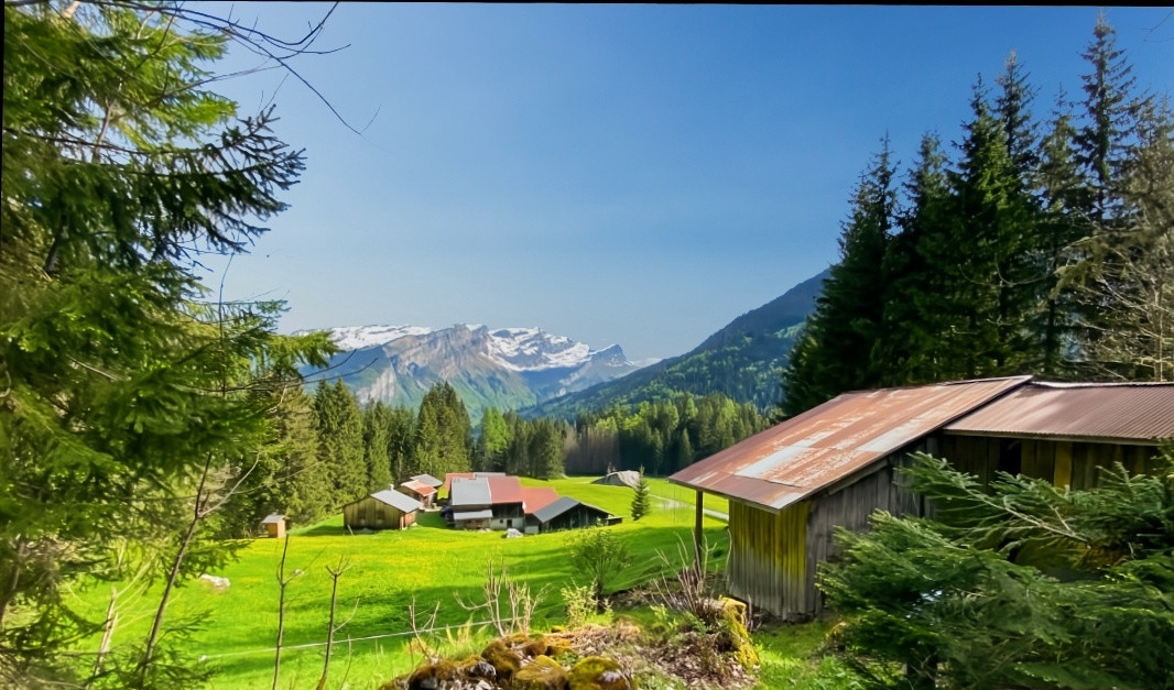 Small wooden cabins sit in a lush green meadow surrounded by pine trees, with snow-capped mountains under a clear blue sky. [AI-generated text]