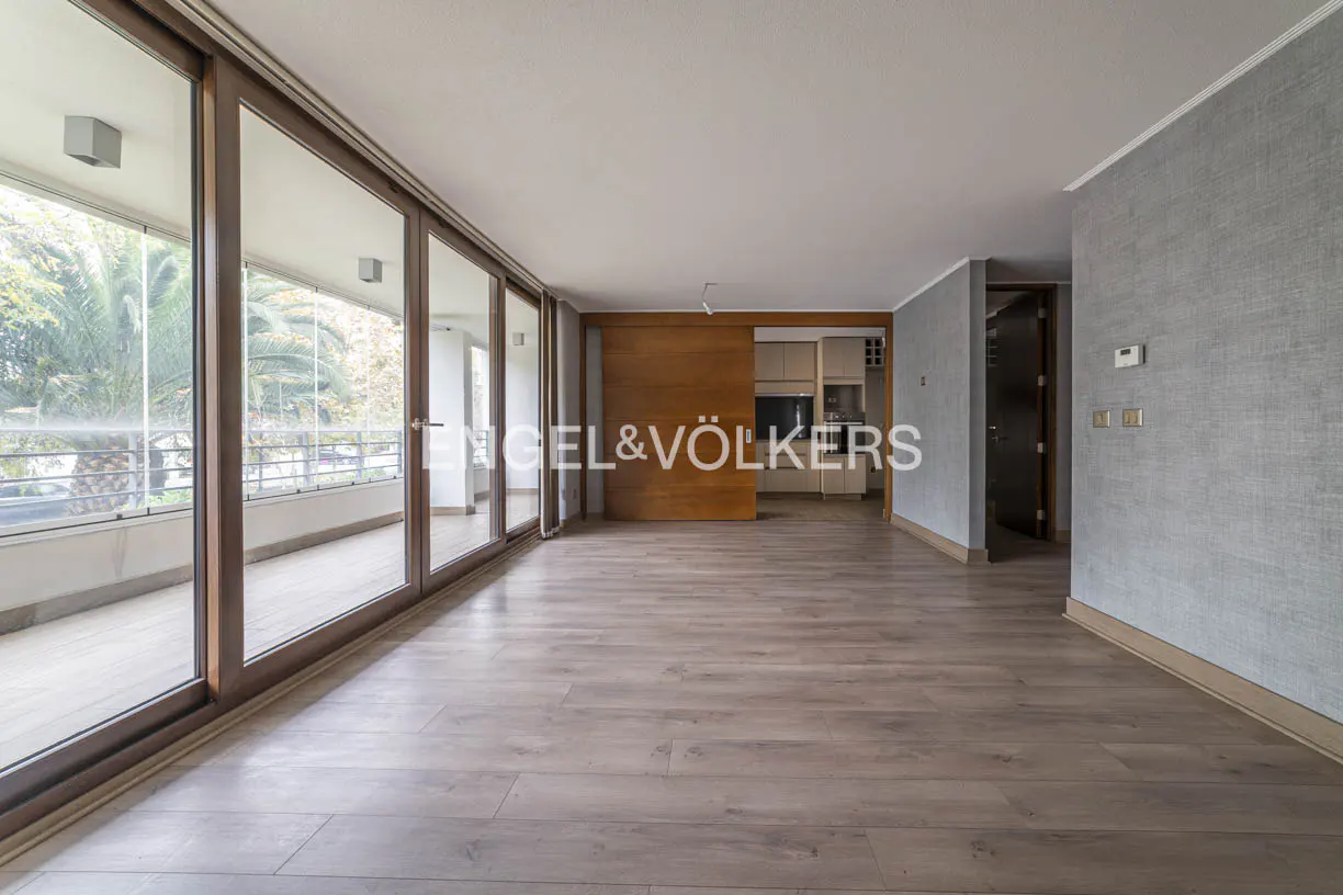 Empty living room with wood floors, large glass doors to a balcony, and a wood sliding door to the kitchen. Gray accent wall.