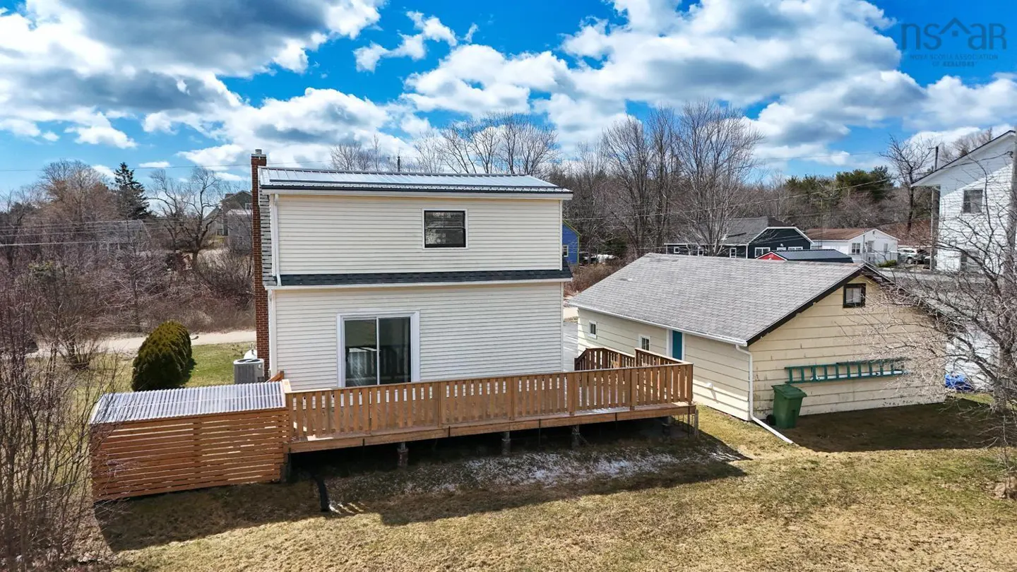 Two-story beige house with a wooden deck and a shed in the backyard under a cloudy blue sky.