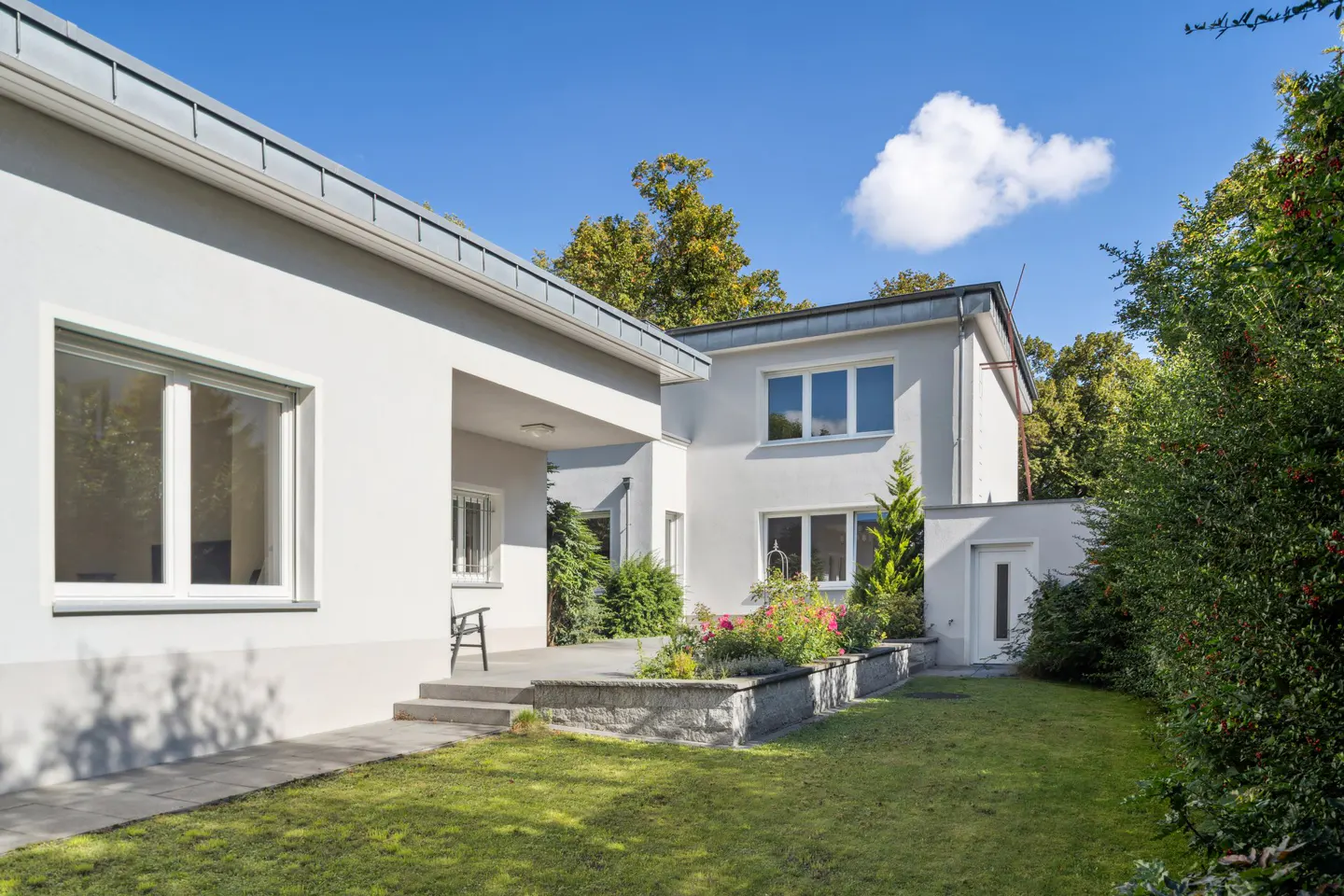 Exterior view of a modern white house with a green lawn, trees, and a blue sky with a white cloud.