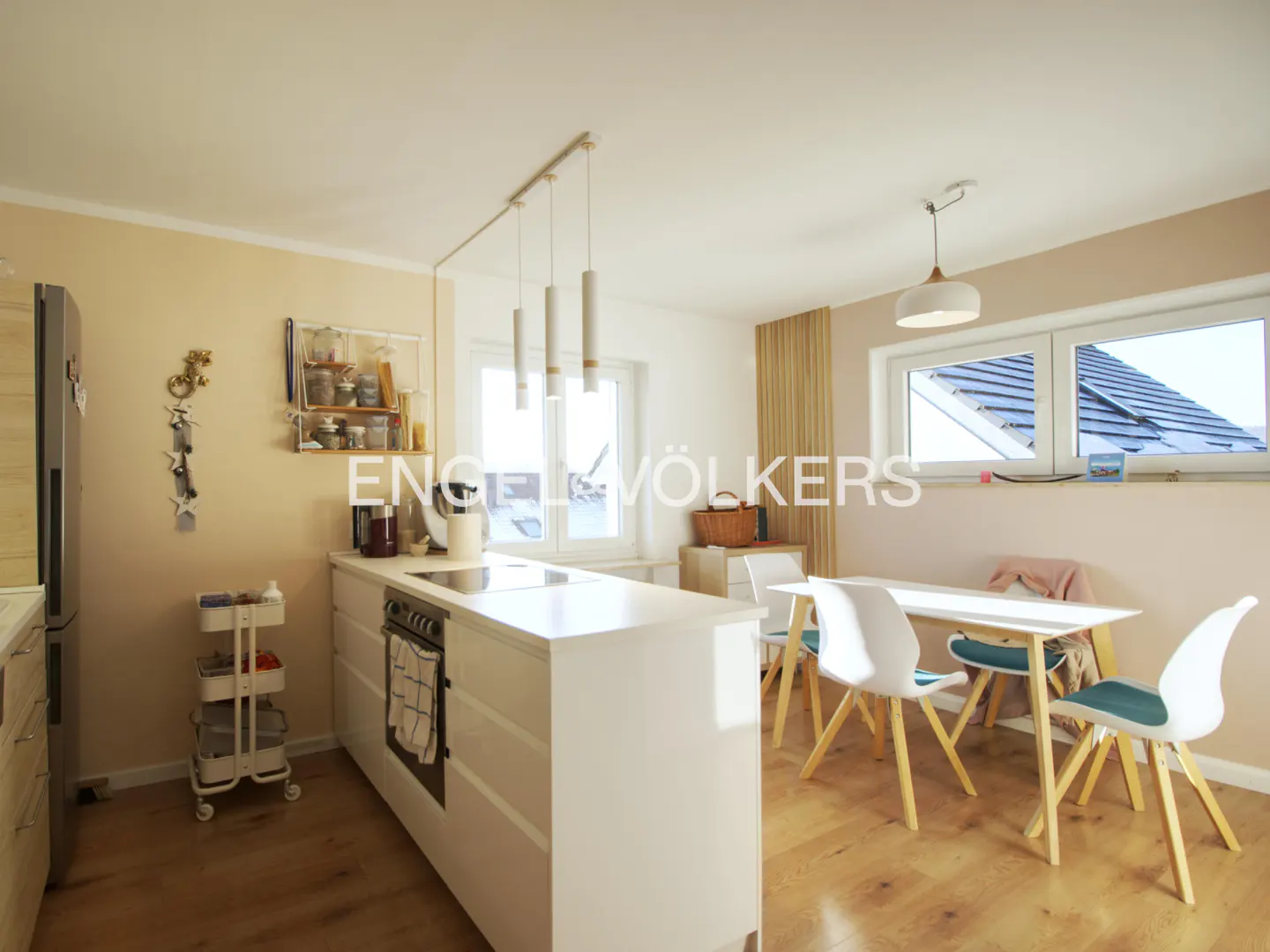 A bright, modern kitchen with white cabinets, a dining table, and wood floors. Natural light streams through the windows.
