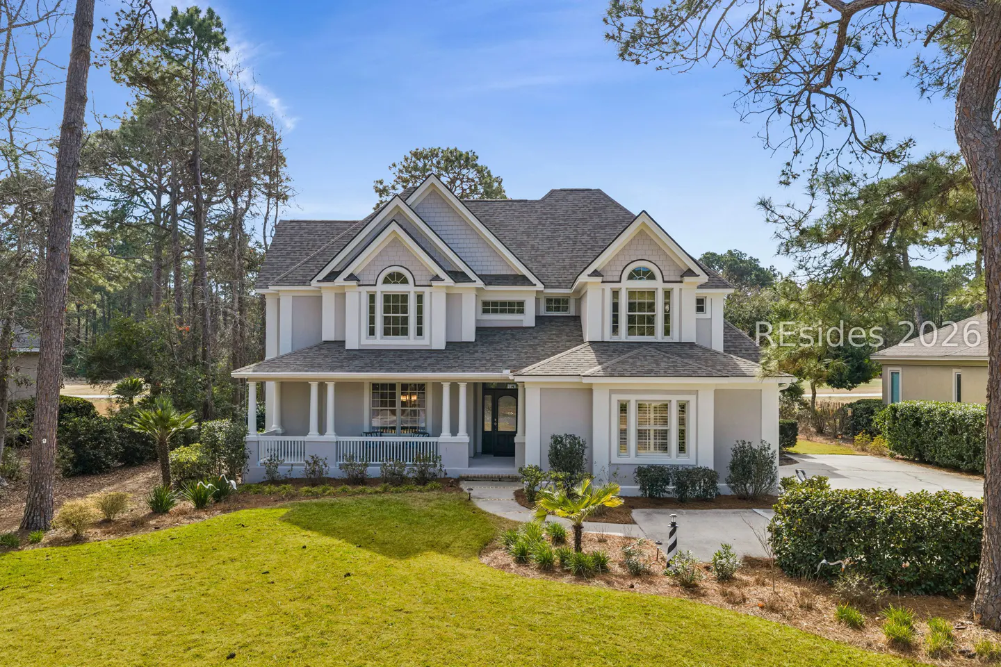 Two-story gray house with white trim, a porch with columns, and a green lawn under a blue sky.