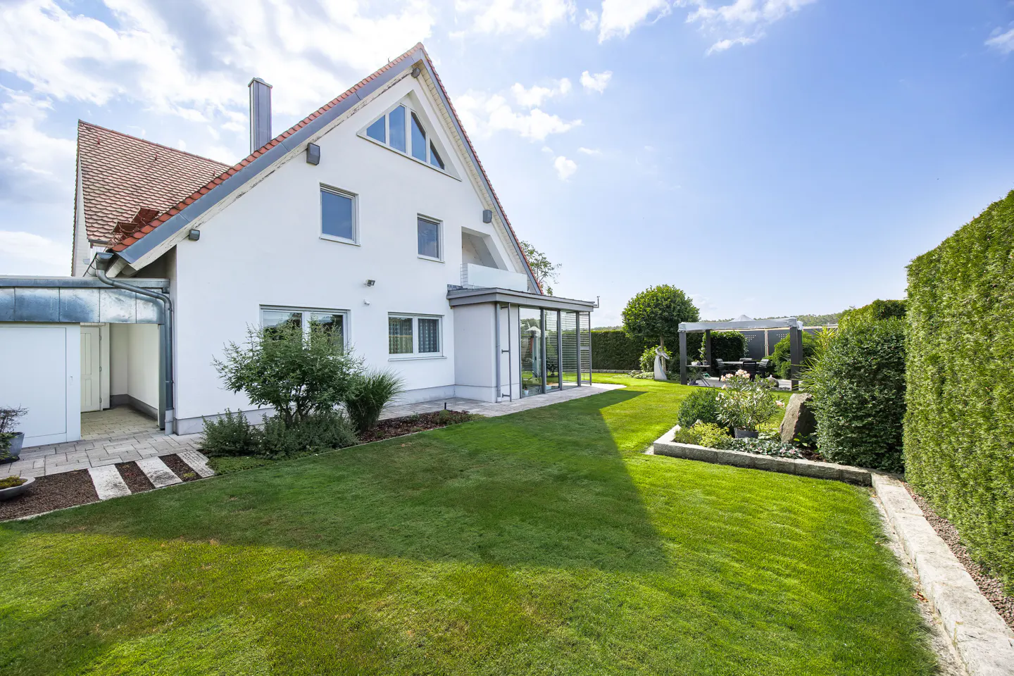 Exterior view of a white two-story house with a red roof, green lawn, and a patio with a pergola.
