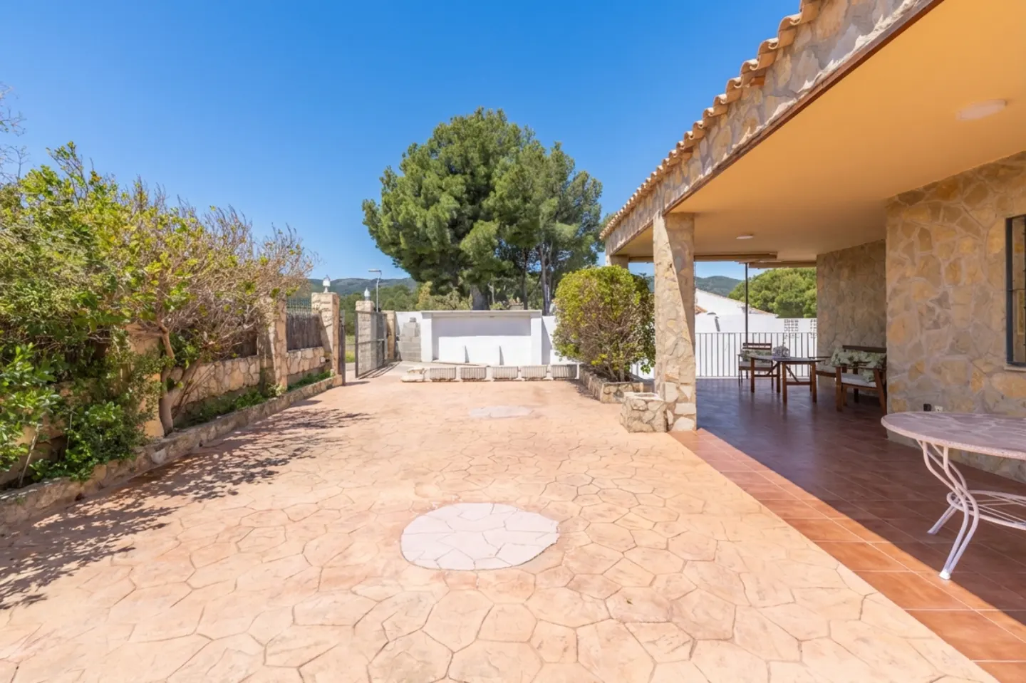 Exterior view of a stone house with a covered patio, a patterned concrete driveway, and a gated entrance.