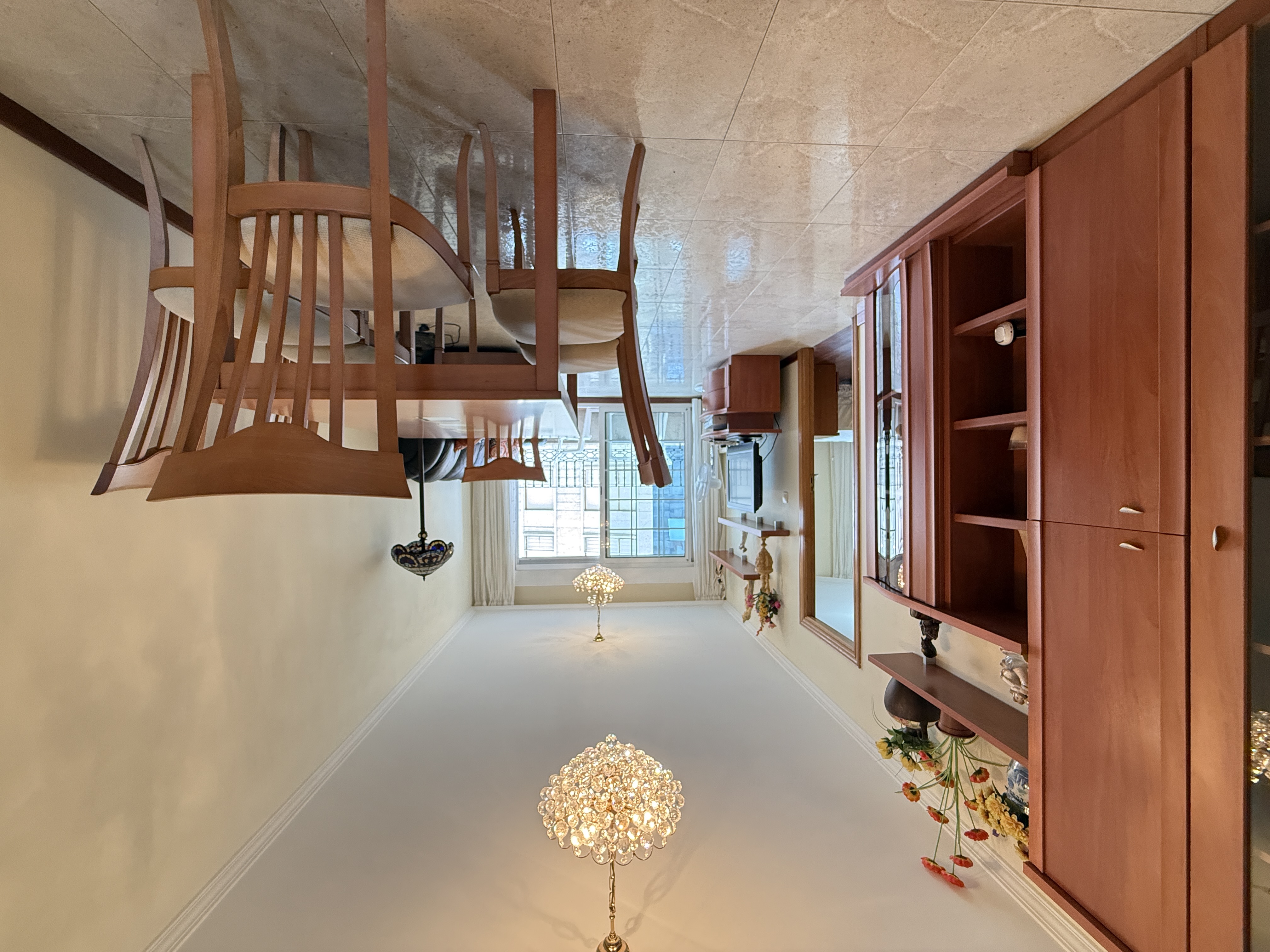Dining area with wooden table and chairs, tile floors, crystal chandelier, and a large wooden storage unit on the left.