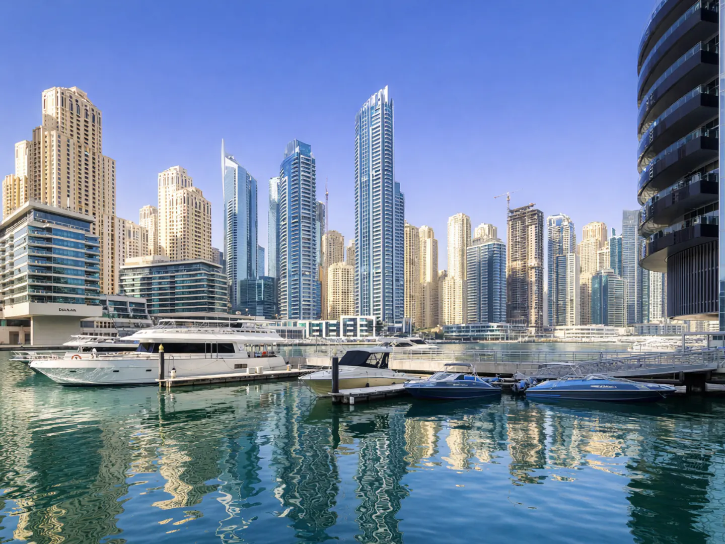 Dubai Marina view with yachts docked in the foreground and skyscrapers in the background under a clear blue sky.