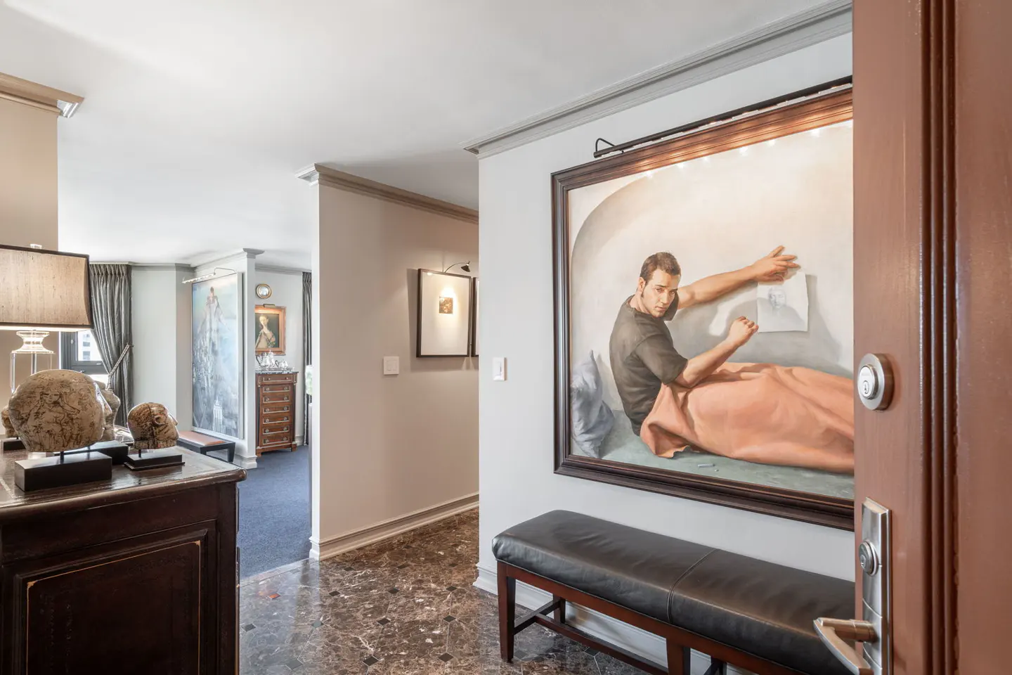 Condo foyer with marble floors, a large painting of a man, and a dark wood bench. A glimpse into the living room is visible.