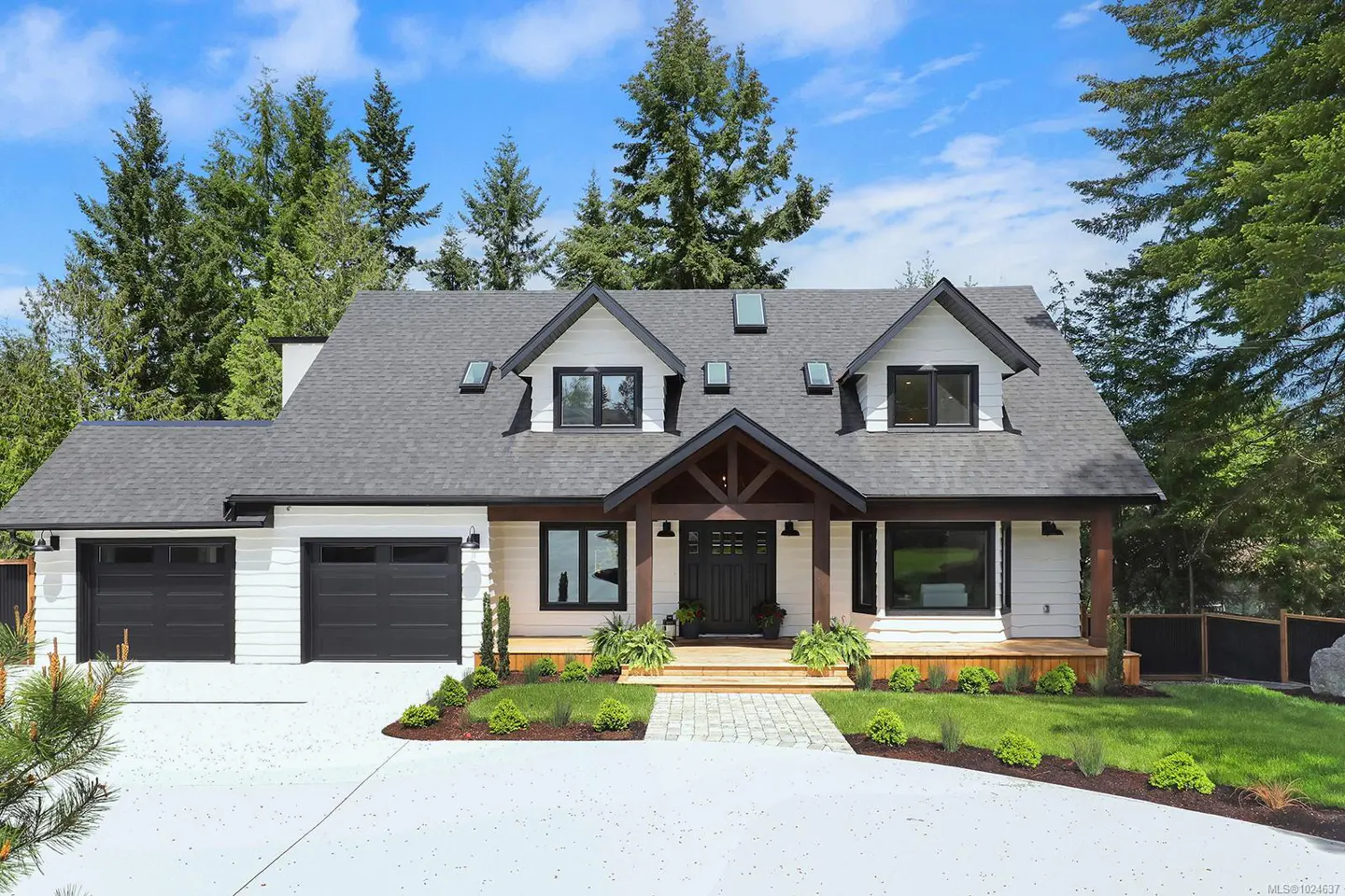 A modern farmhouse with white siding, black trim, and a gray roof, surrounded by green trees and a blue sky.