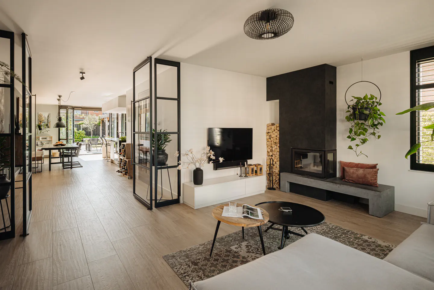 Bright living room with wood floors, black framed glass doors, fireplace, TV, and two coffee tables.
