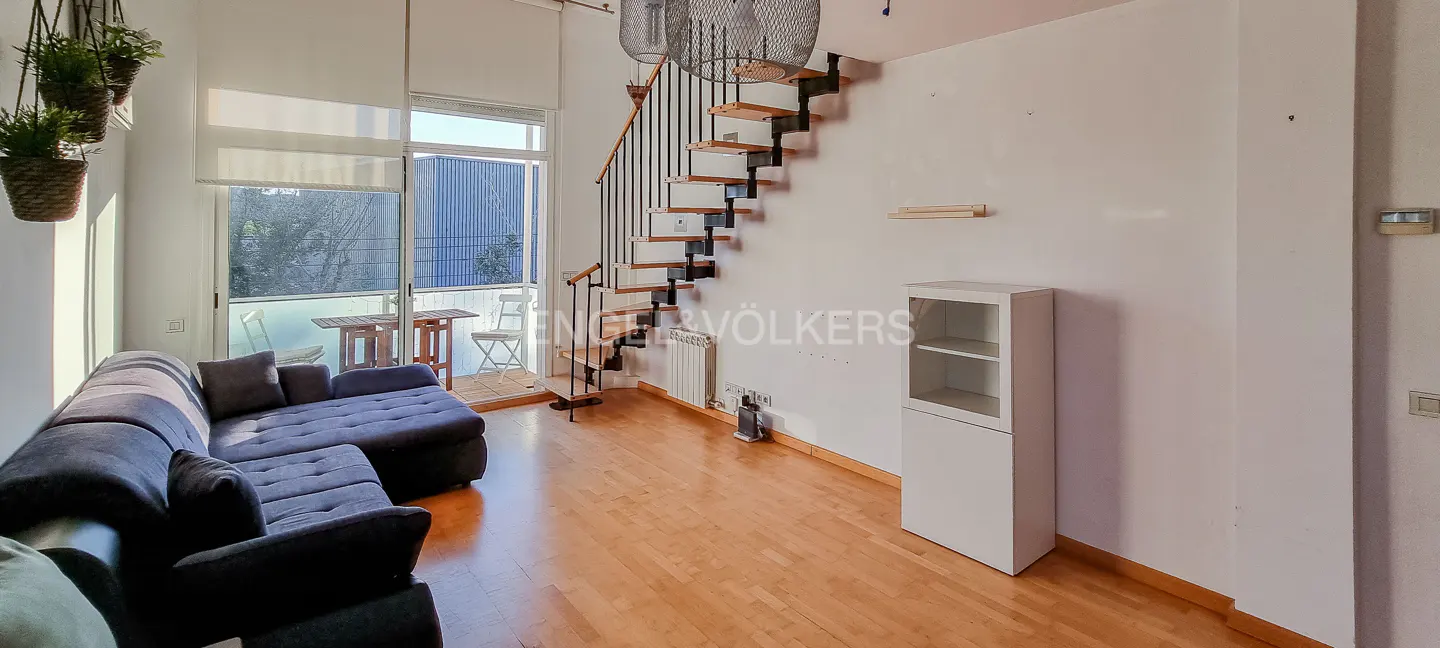 Living room with a blue sectional sofa, wooden floors, and a staircase leading to the upper level. Balcony with table and chairs.