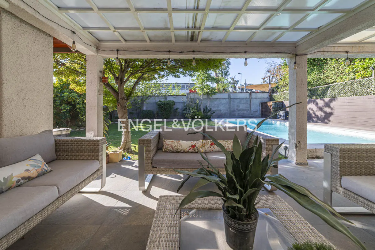 Covered patio with wicker furniture overlooks a pool and backyard. A potted snake plant sits on a wicker table.