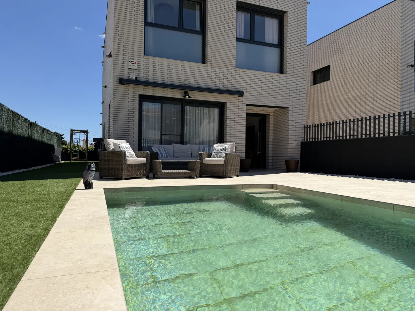 Backyard view of a modern two-story house with a pool, patio furniture, and green grass.