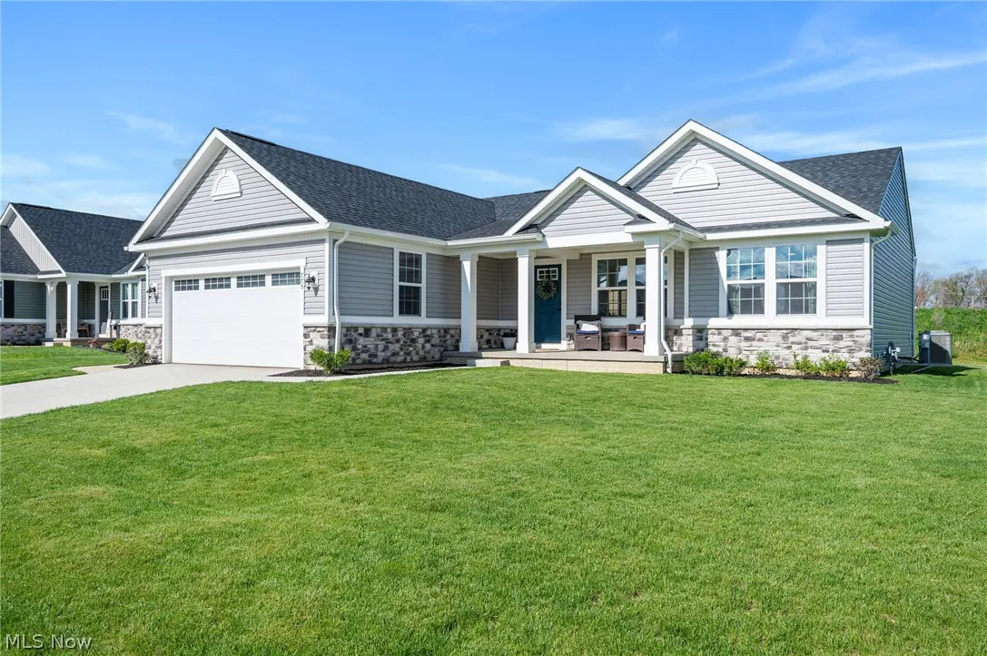 A single-story home with gray siding, a dark roof, and a teal front door. A green lawn stretches to the street.