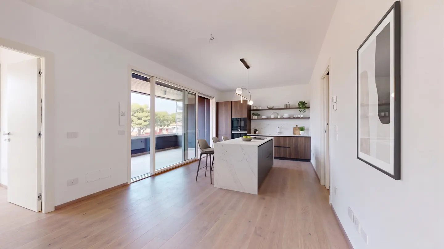 Bright, modern apartment interior with wood floors, white walls, and a kitchen island. Sliding glass doors lead to a balcony.