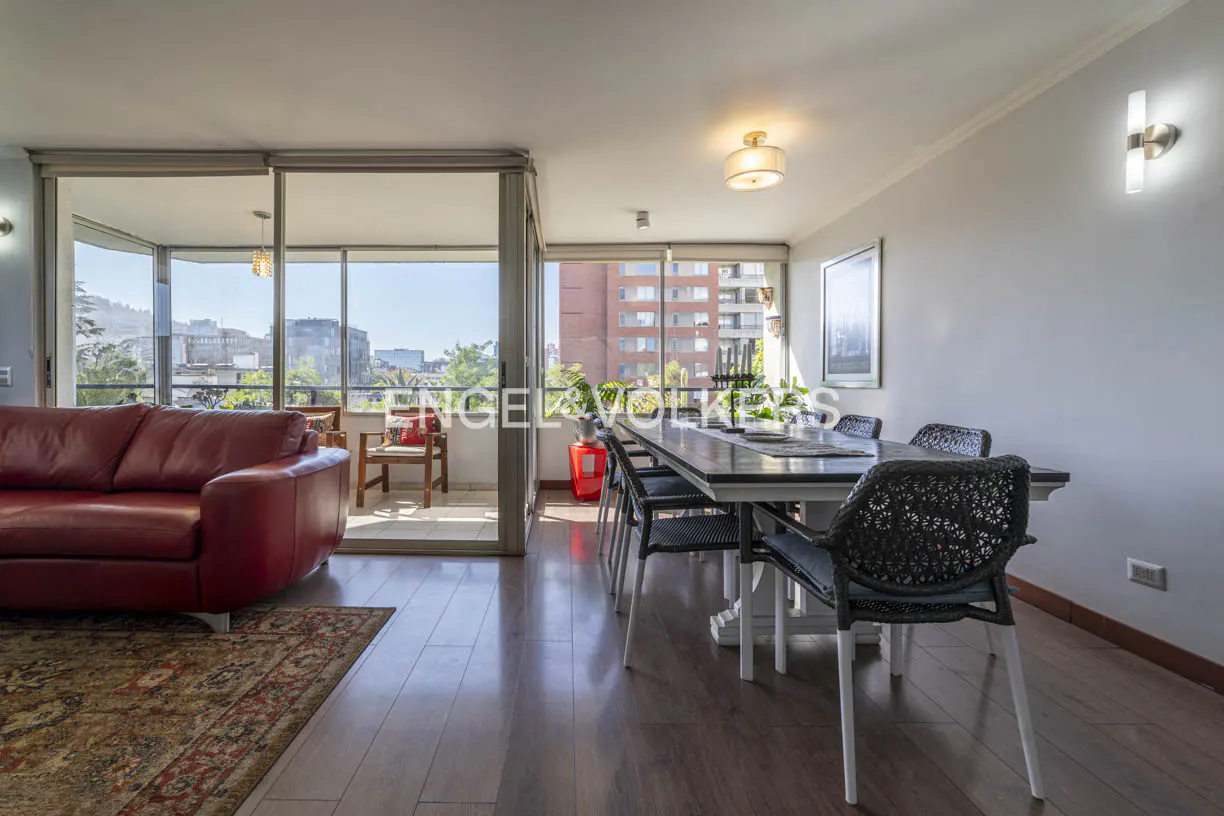 Bright living room with a red leather sofa, a dining table with black chairs, and a balcony overlooking a city.