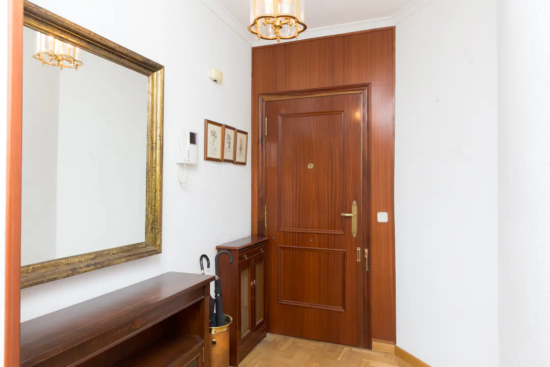 Entryway with a wood door, gold framed mirror, and a console table. An umbrella stand and wall art add to the decor.