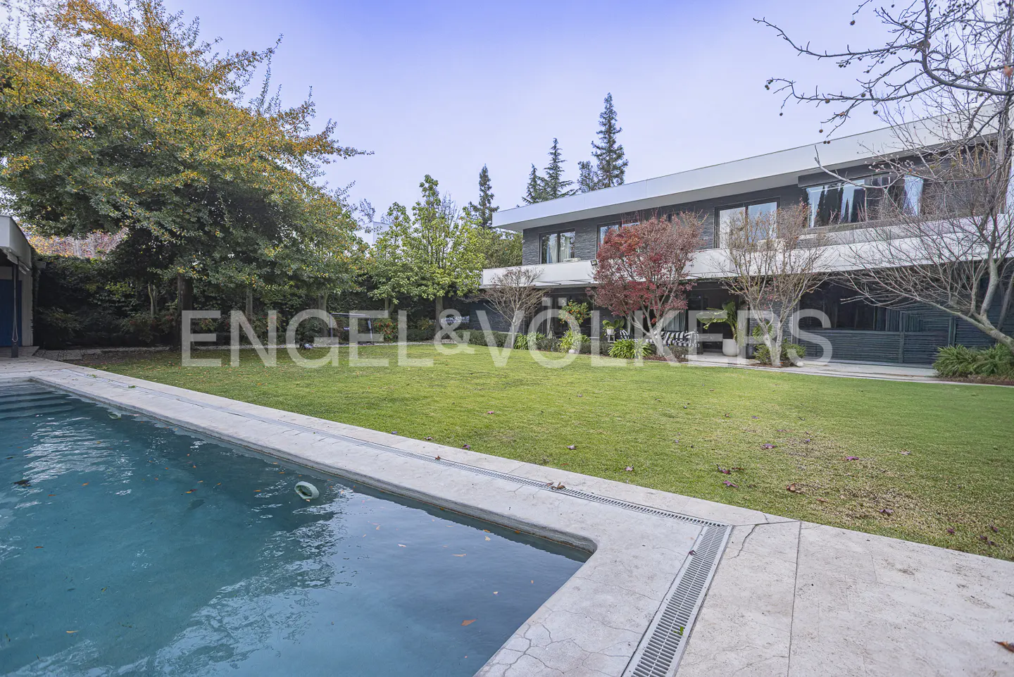 Modern two-story home with a large green lawn, swimming pool, and mature trees in the backyard.