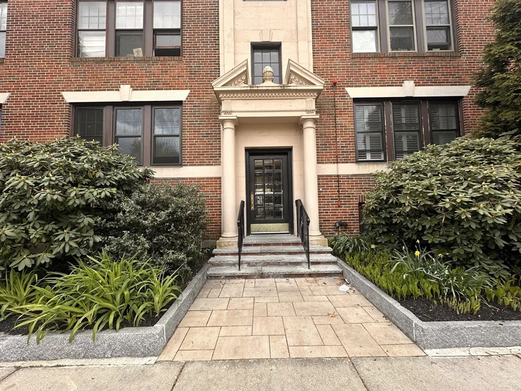 Brick apartment building with a black front door framed by stone columns and a stone walkway leading to the entrance.